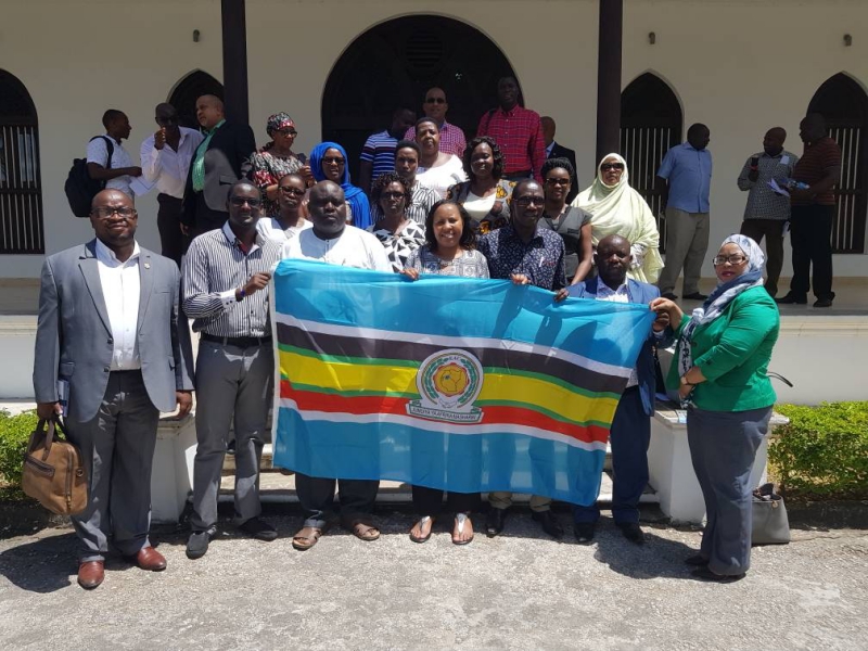 A section of Members who were in Zanzibar at the start of the tour of the Central Corridor present the EAC flag to the Executive Secretary of the East African Kiswahili Commission (EAKC), Prof K. Simala (centre in white shirt).  Leading the delegation is Hon Wanjiku Muhia (next to the EAKC Executive Secretary)  