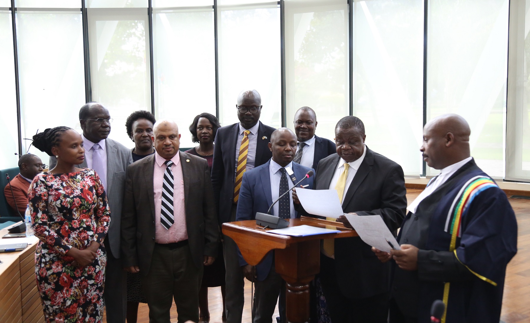 Hon. Major General (Rtd) Kahinda Otafiire taking Oath of Allegiance as an Ex-Officio Member of the Assembly flanked by several Members.