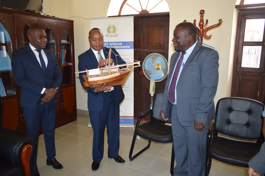 EAC Secretary General Hon. Dr. Peter Mathuki admires a gift in the form of dhow that he received from the Acting Executive Secretary of the East African Kiswahili Commission, Dr. James Jowi (right). Looking on is Hon. Mudrik Soroga, Zanzibar's Minister of State for Labour, Economy and Investment. The dhow signifies Zanzibar's blue economy and the Secretary General's stewardship of the Community.